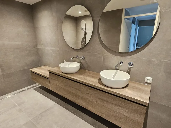 Badkamer met houtlook badmeubel, twee ronde spiegels en warme tegels