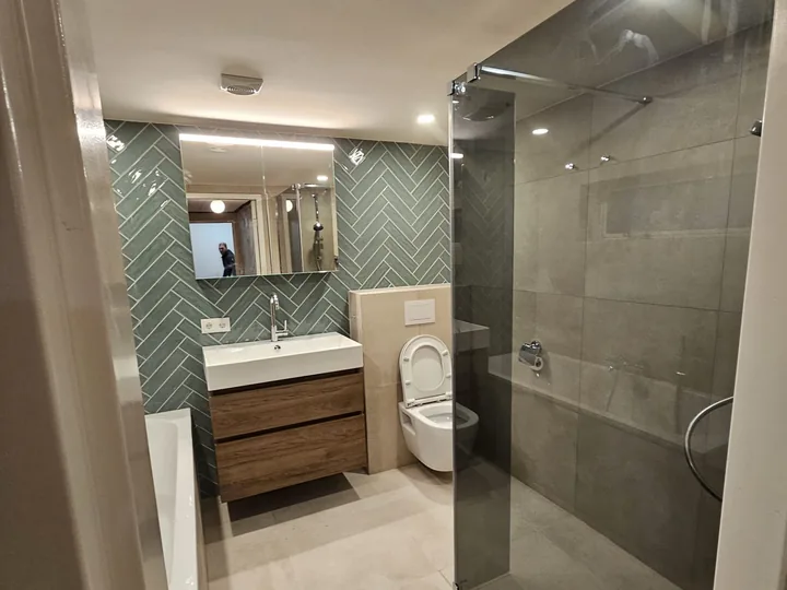 Badkamer met groene visgraattegels, ligbad en badmeubel van walnoot