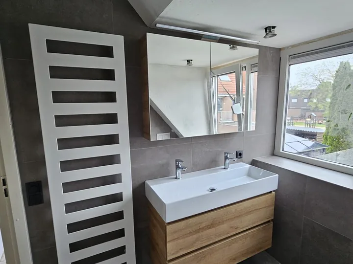 Witte designradiator naast een zwevend badmeubel met grijze tegels